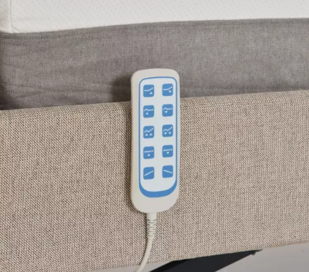 A close-up of a white electric blanket controller with blue buttons, attached to a cord and resting on a beige textured fabric surface.