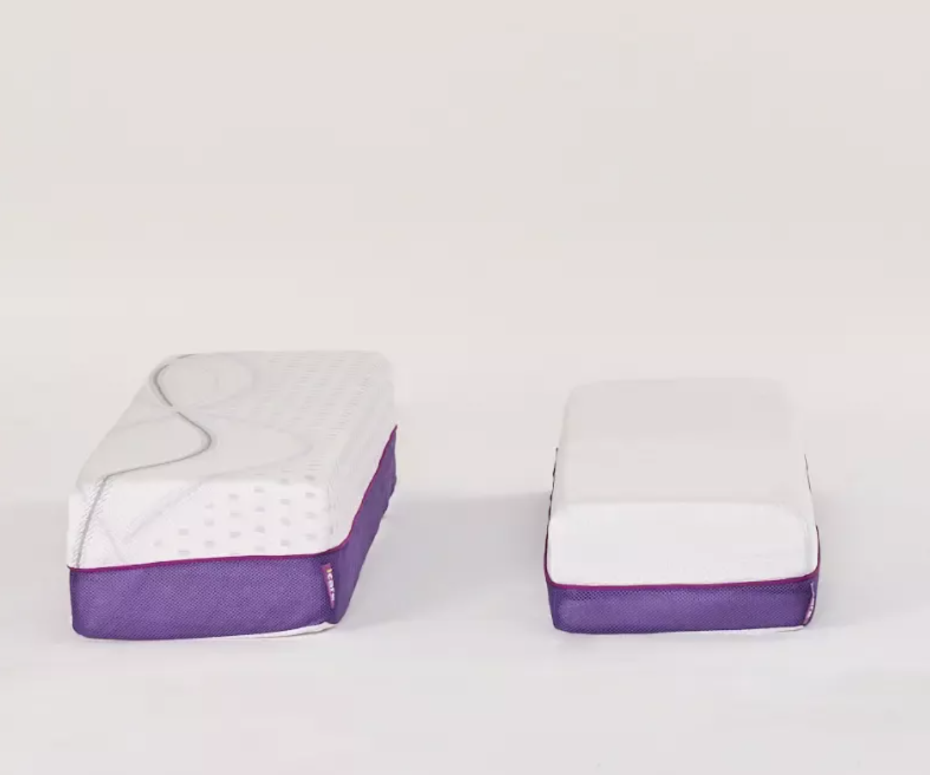 Two white rectangular mattress or cushion-like products with purple fabric sides, shown side by side on a clean white studio background.