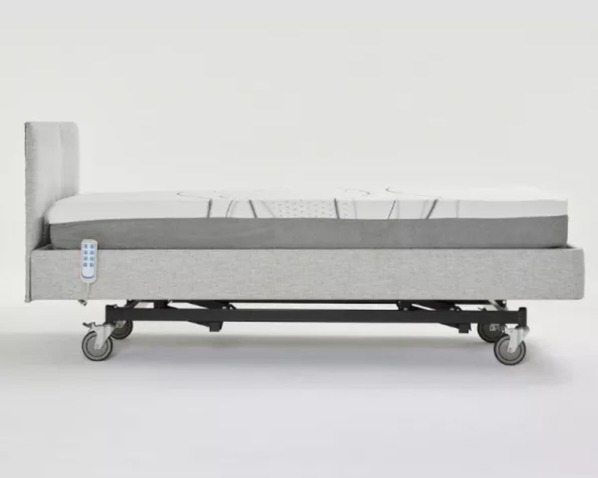 An electric hospital bed with a light gray upholstered frame, a white mattress, and a black wheeled base, shown from a side profile against a white studio background.
