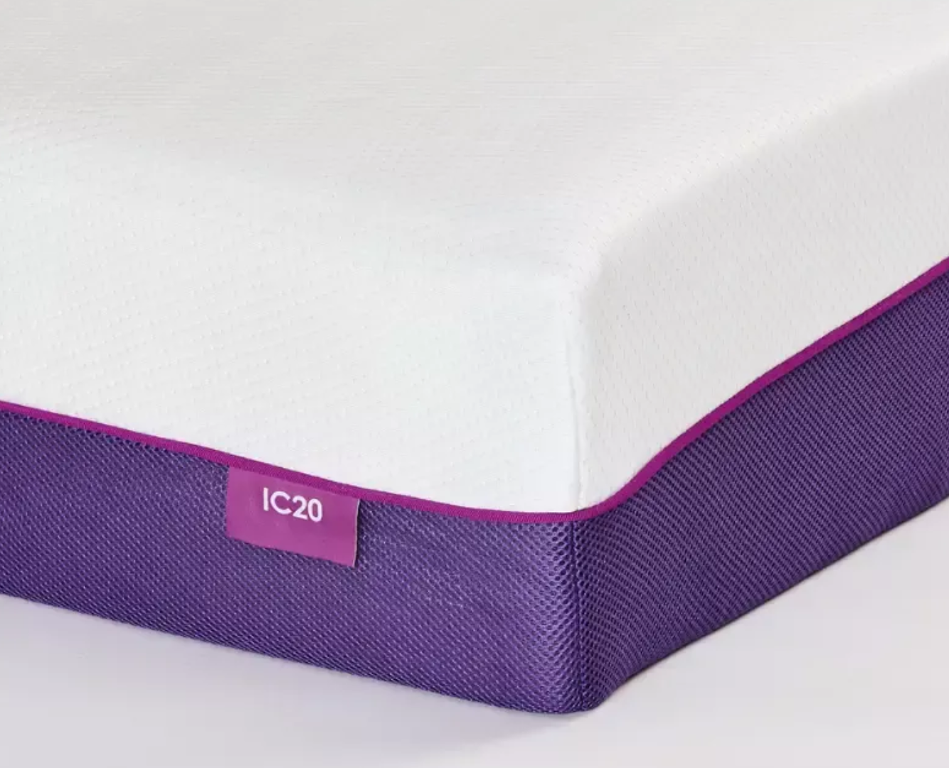 A close-up of a mattress corner showing a white top surface, a purple side skirt, and a small purple label reading IC20.